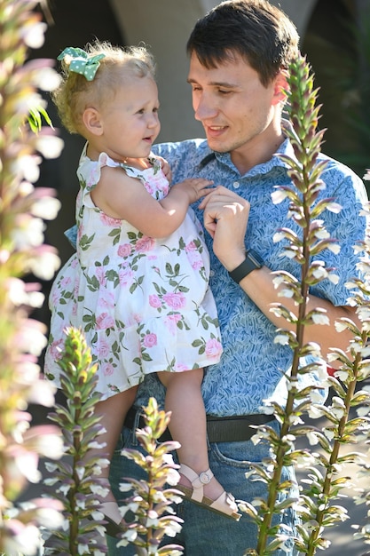 Father holds baby daughter in white dress and smiles Father's Day Daddy's Day Sunny day