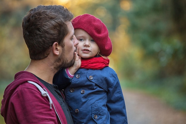 Photo father hugs and kisses daughter in the autumn park they laugh and walk