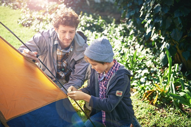 Father kid and set up tent for camping outdoor in nature on vacation while bonding in summer Dad boy and preparing campsite learning and getting ready in forest for travel education and holiday