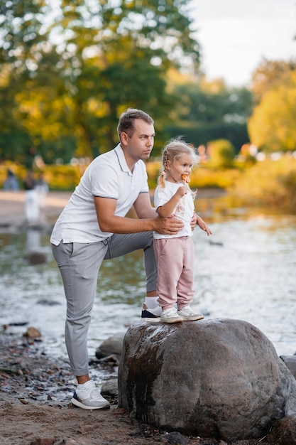 Father and little cute blond daughter together in the summer in the park in nature little girl eating lollipop