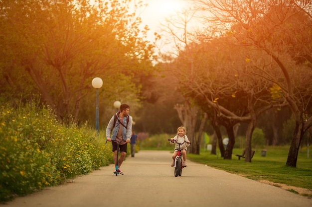 Father and little daughter riding scooter and bike, family sport