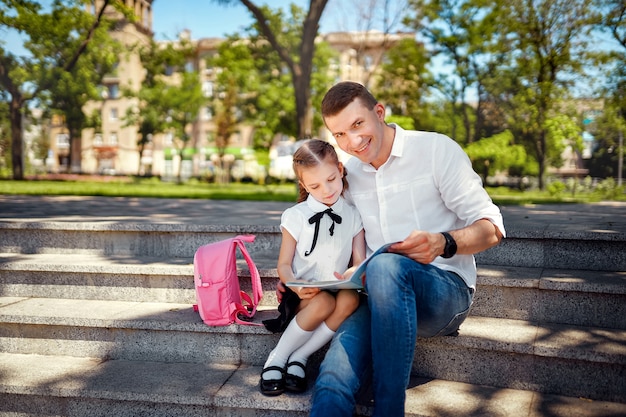 Father and little daughter sitting on stairs and read book