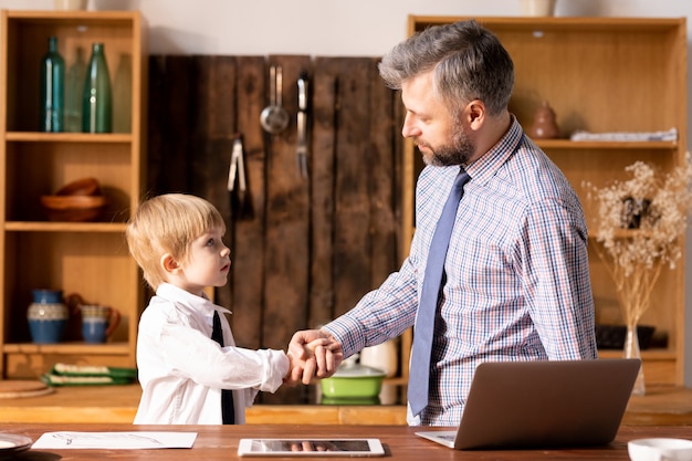 Father making handshake with little son in formal shirt