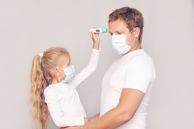 Father in a medical mask measures his daughter's temperature with an electronic thermometer on an isolated background