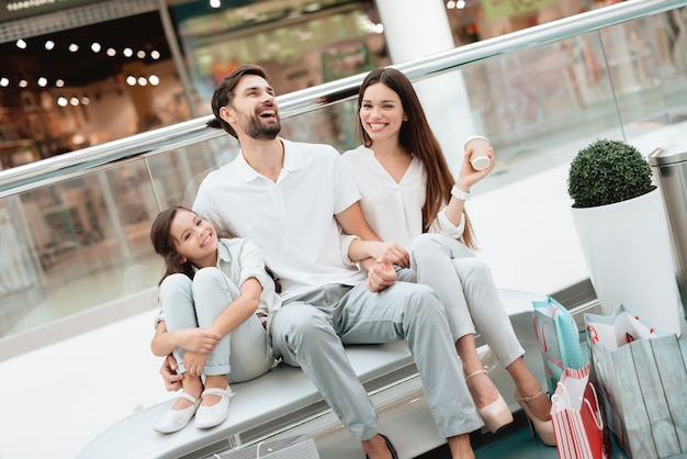 Father, mother and daughter are sitting on bench in mall.