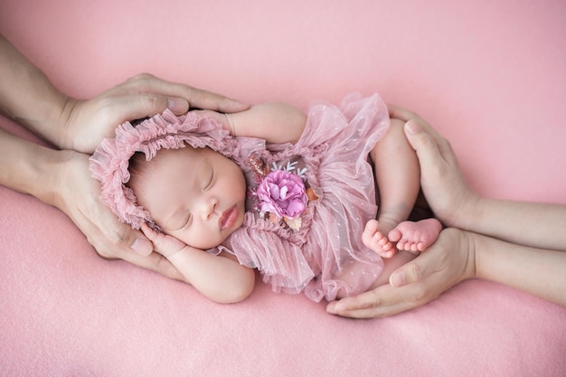 Father and mother hand holding adorable cute Asian newborn baby sleeping on pink background