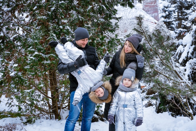 Father and mother hold children in their arms laughing cheerfully family winter walk in forest raisi...