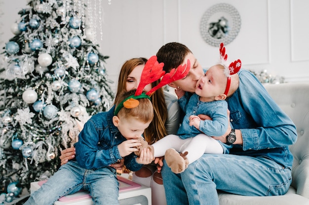 The father, mother holds little son and daughter near Christmas tree.