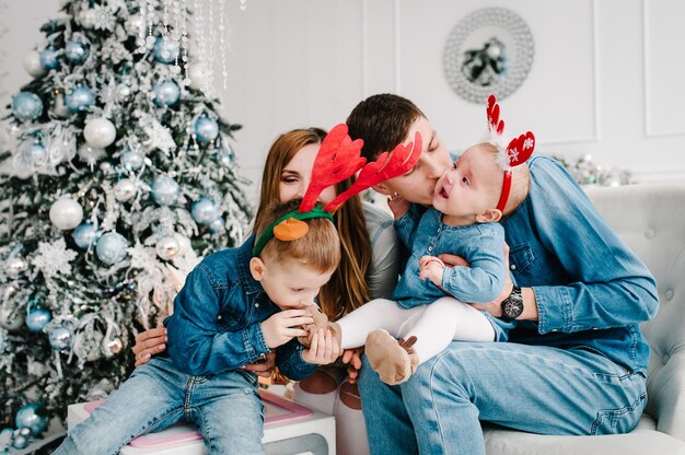 The father mother holds little son and daughter near the Christmas tree