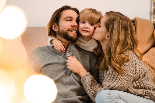 Father and mother hug and kiss their beloved daughter while sitting on the sofa