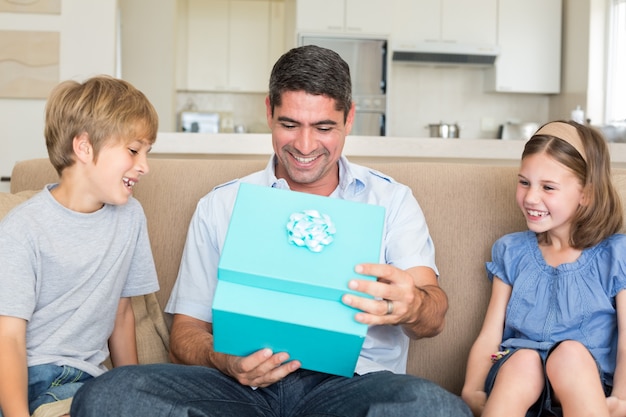 Father opening gift given by children on sofa