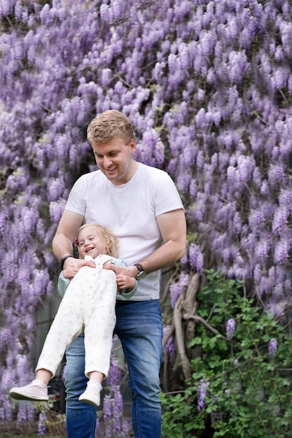 Father playhaving fun outdoor with baby girldaughter on background of glucinum flowerpurplevery peri