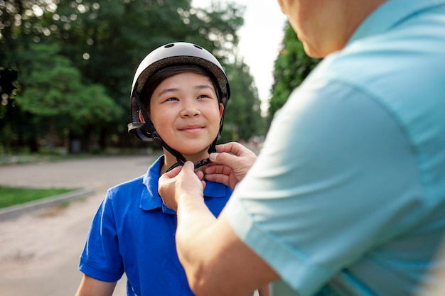 father puts protective helmet on his Asian son's head Korean boy rides bike with dad in the park