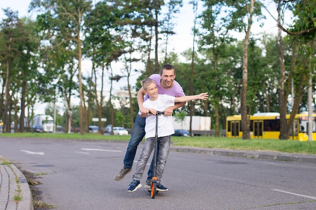 A father rides his son in a white Tshirt on a scooter the happy child spread his hands