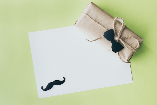 Father's day. Gift package wrapped with paper and rope with a decorative bow-tie on green background. Copyspace