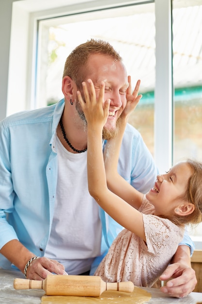 Father showing his little daughter how to roll dough for cookies