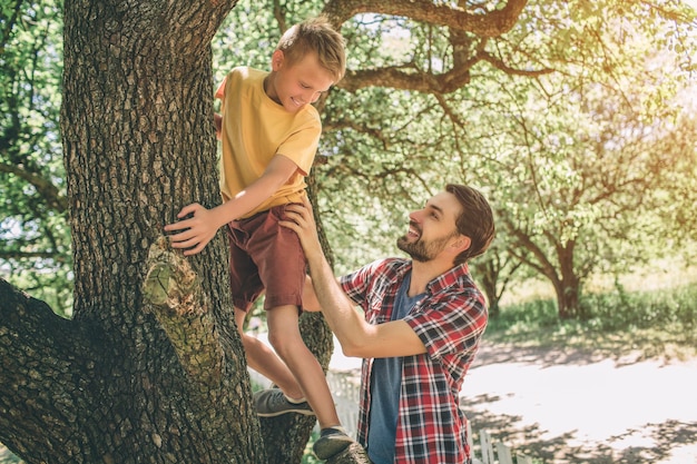 Father and son are playing with each other. Guy is supporting his child. Boy is looking down at father. They are smiling. Both of them are happy