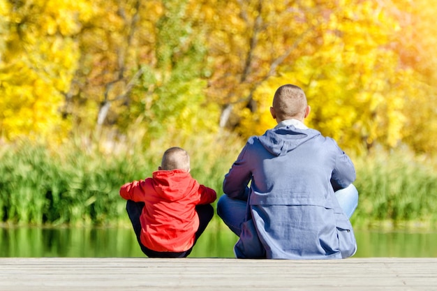 Father and son are sitting on the dock Autumn sunny Back view