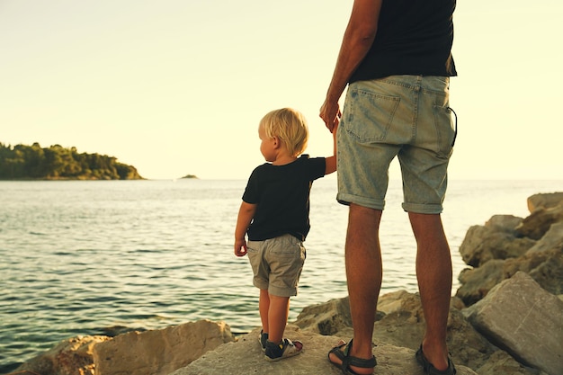 Father and son back silhouettes walking by the sea Man and kid boy playing together outdoors on a sea beach Loving family and summer vacation