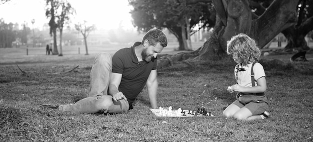 Father and son play chess on grass in summer park family