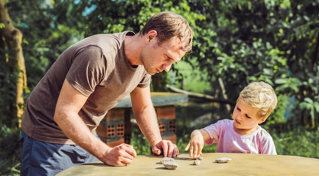 Father son play outside sun day show explain driving traffic regulation rules use stone imitation cars Instruction hand palm finger gesture Expressive Serious face expression Home child education