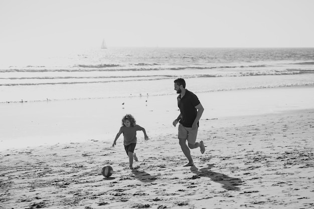 Father and son play soccer or football on the beach happy family concept