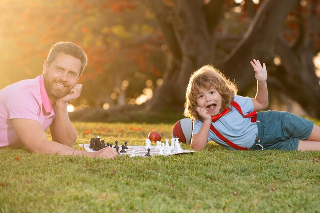 Father and son playing chess lying on grass at lawn park games and entertainment for children family