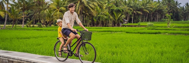 Father and son ride a bicycle on a rice field in ubud bali travel to bali with kids concept banner