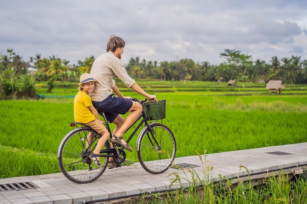 Father and son ride a bicycle on a rice field in ubud bali travel to bali with kids concept