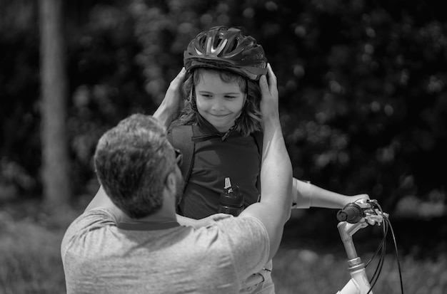 Father and son riding bike in park child in safety helmet with father riding bike in summer day