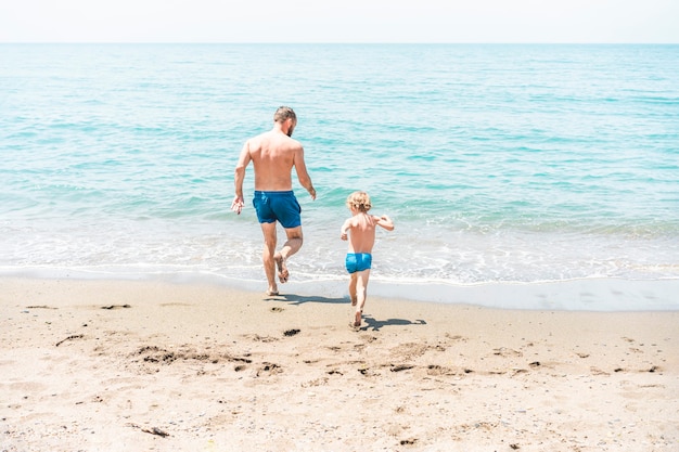 Father and son running towards the ocean together during summer vacation