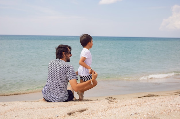 Father and son sit on the beach with sand in summer while on vacation