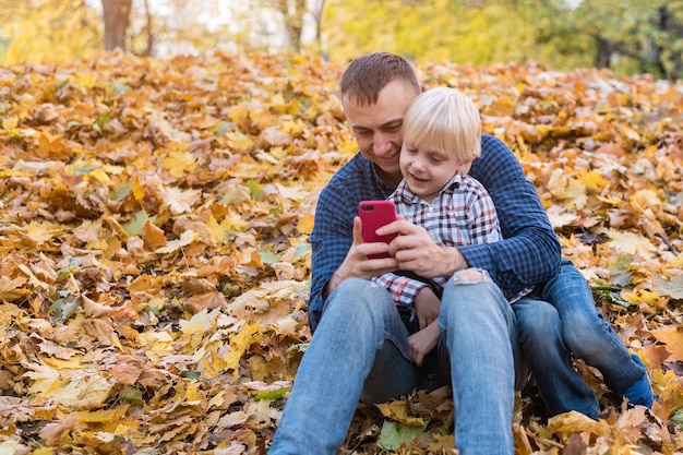 Father and son sitting in autumn Park and looking at phone Fatherhood