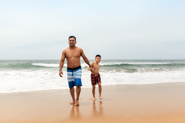 Father and son walking on the beach in summer shorts, travel and family vacation concept