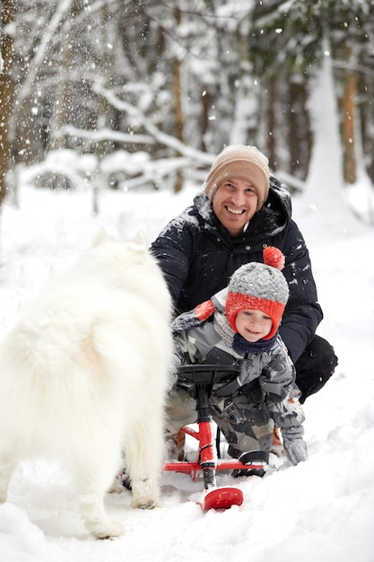 Father and son walking in snowy forest with his beagle dog in pine forest Family walking with pets and winter outfit concept image