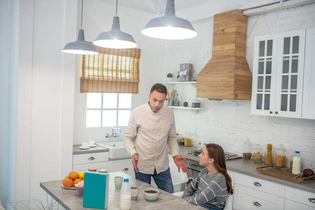 Father talking about the benefits of good nutrition, located near the kitchen table, his daughter sitting at the table