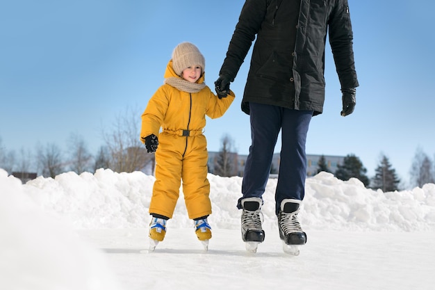 A father teaches a child to skate at a rural outdoor skating rink holding her hand