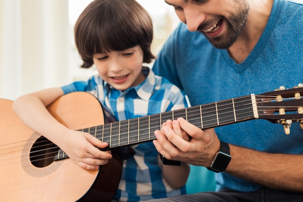 The father teaches his son to play the guitar