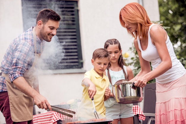 Father teaching children to barbecue food at yard