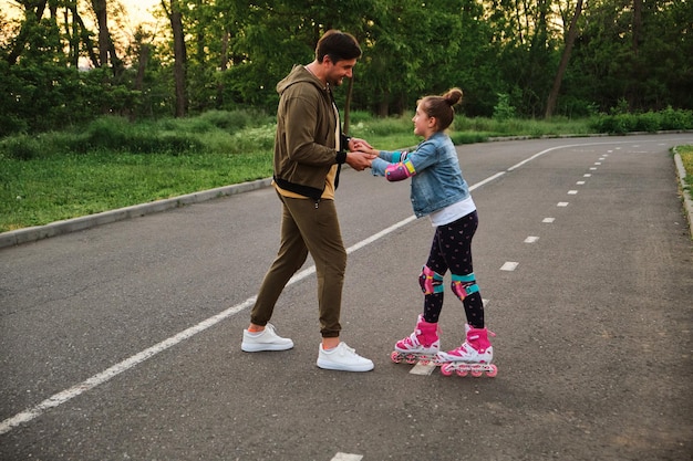 A father teaching his daughter roller skating in a park on summer day