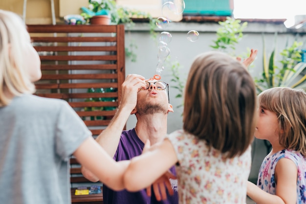 Father and three female children outdoor playing bubble soap - togetherness, happiness, bonding concept