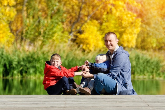 Father and two sons play on the dock Autumn sunny Side view