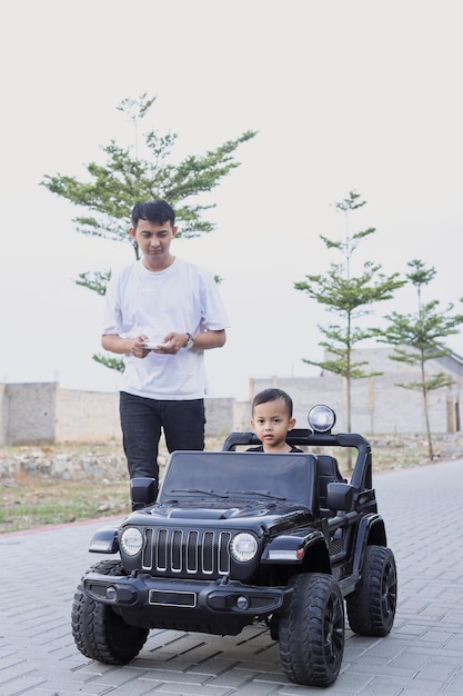 Father watching cute boy driving in little car and controlling remote.