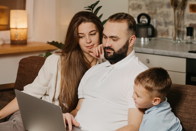 Father with a beard who is showing his achievements at work on a laptop to his son and pensive wife at home