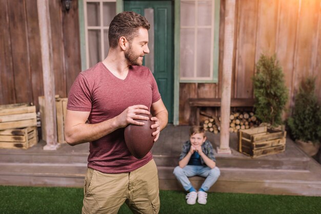 Father with little son playing american football with ball at backyard dad and son playing