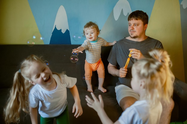 Father with many children has fun playing with his small children at home blowing soap bubbles