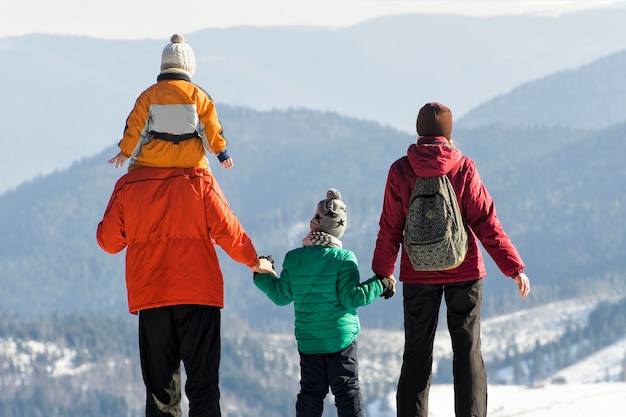 Father with son on shoulders mother and son stand back against the background of snowcapped mountains Winter sunny day