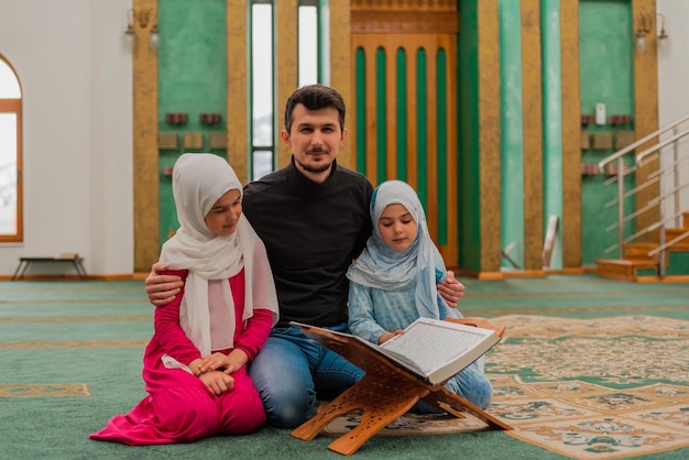 Father with two child daughters reading a holy book Quran inside the Mosque Happy Muslim family