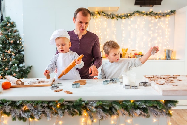 Father with two kids cooking making gingerbread, cutting cookies of gingerbread dough, having fun.