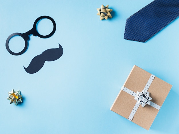 Fathers day concept with gift  box, tie and mustache on blue background